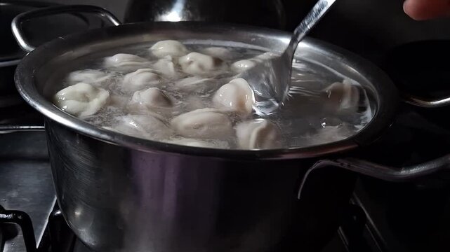 process of boiling homemade pelmeni in a silver pot on a home stove