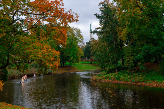 Autumn Park With River, Fountains and Distant Statue Monument Under Overcast Sky