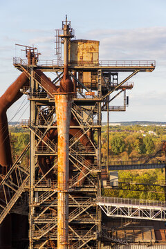 Vertical photo of historic blast furnace upper steel superstructure with rusty conical pipe high catwalk platforms observation deck and green forest canopy in Duisburg Ruhr region Germany