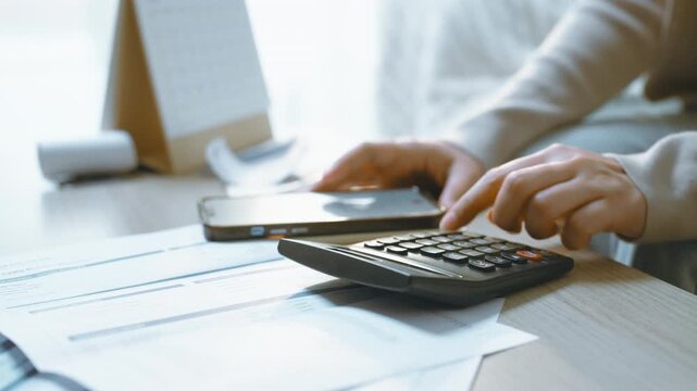 Expense calculation with a calculator over a statement, a hand pressing the keys as the calculator fills the frame, with statement details beneath it and a smartphone resting unused farther back.