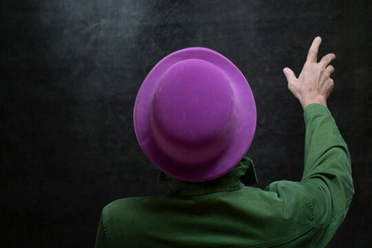 Man in a green shirt and a purple hat points upward with his finger.