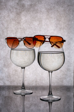 Figure with glasses containing liquid, along with a pair of sunglasses, on a gray background