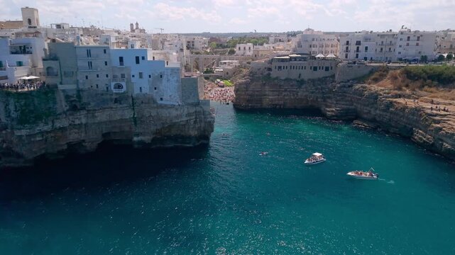 Polignano a Mare Puglia drone. White cliffside town, Lama Monachile iconic beach gorge reveal, Adriatic sea panning panorama. Authentic Italian coast travel 4K video.