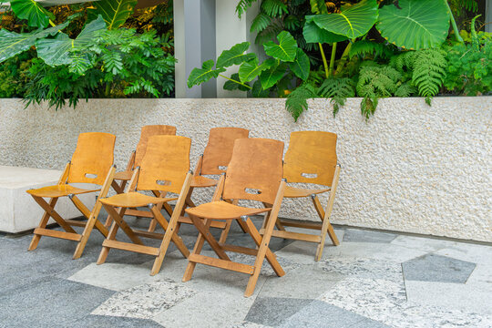 Empty wooden folding chairs arranged beside textured stone wall and tropical greenery in Shenzhen, China. Outdoor seating, hospitality furniture, tropical landscape design, waiting area