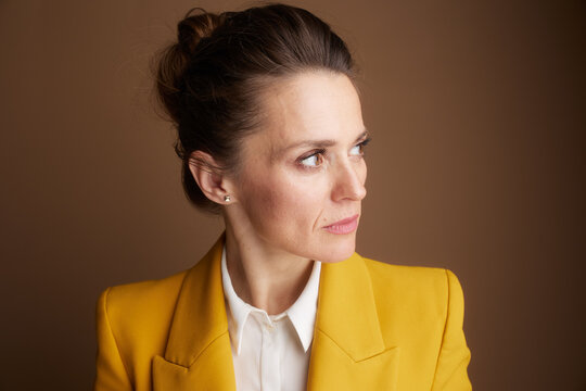 A professional woman in a vibrant yellow blazer looks thoughtfully to the side, her focused expression conveying deep concentration or strategic contemplation in a corporate setting.