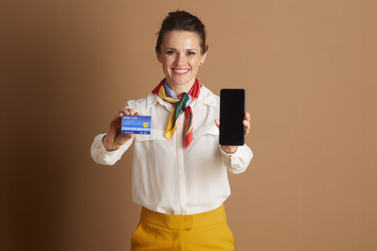 A confident business woman in a white blouse and yellow pants showcases a credit card and smartphone, embodying modern digital payments and financial convenience.