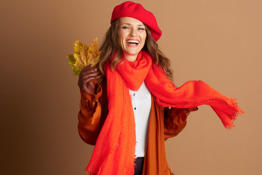 Joyful woman, long brown hair, red beret, orange scarf, and jacket, laughs delightfully holding vibrant autumn leaves. Dynamic medium shot captures happy moment celebrating fall season.