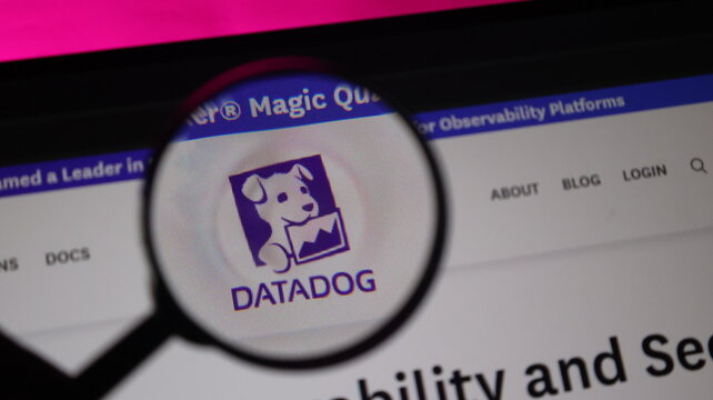 Datadog logo under magnifying glass on monitor screen symbolizes cloud monitoring and observability platform analysis for application performance and data metrics.