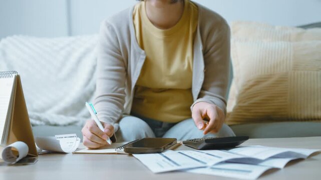 Household budget notes in a notebook, with a person writing beside a calculator and pressing its keys, the notebook open among statements and receipts as writing accompanies the financial review.