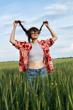 Woman in sunglasses lifts her long hair while standing in green field.