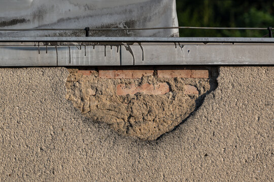 Exposed red bricks under fallen plaster on a house wall.