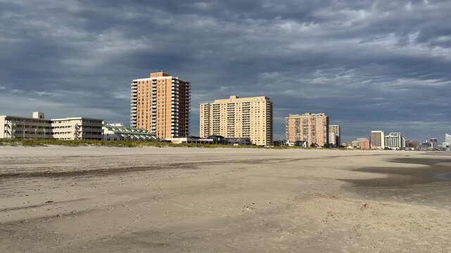 Pan view of tall and buildingd and short motels along the shoreline by the beach. The skyline of Atlantic city is also scene