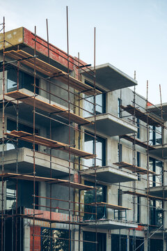 Vertical low angle shot of a multistory building under construction surrounded by metal scaffolding and wooden walkways.