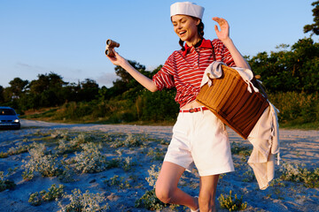 Smiling woman with binoculars and picnic basket on beach at sunset. Lifestyle theme, travel concept, vintage style clothing, summer outdoor leisure activity, nature landscape view. © SHOTPRIME STUDIO