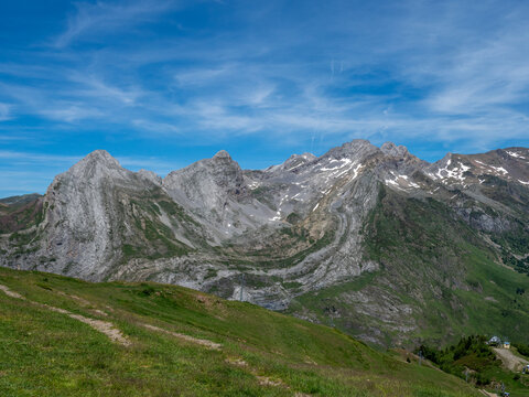 Pyrenees Mountain Peaks Summer Landscape - Rocky Pyrenees mountain peaks with residual snow patches, green alpine meadow foreground and blue sky in summer.