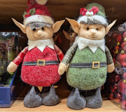 Tiempo de Navidad. Simp&aacute;ticos mu&ntilde;ecos de peluche de elfos de Santa Claus con ropa en color verde y en color rojo, rodeados de decoraci&oacute;n navide&ntilde;a, de pie en el estante de una tienda 