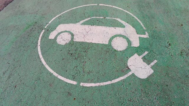 Electric vehicle charging station sign painted on green asphalt parking lot