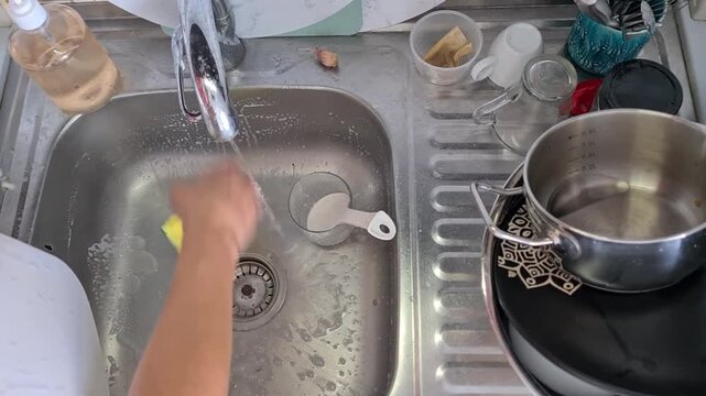 Person washing a yellow dish with a sponge in a kitchen sink during dishwashing