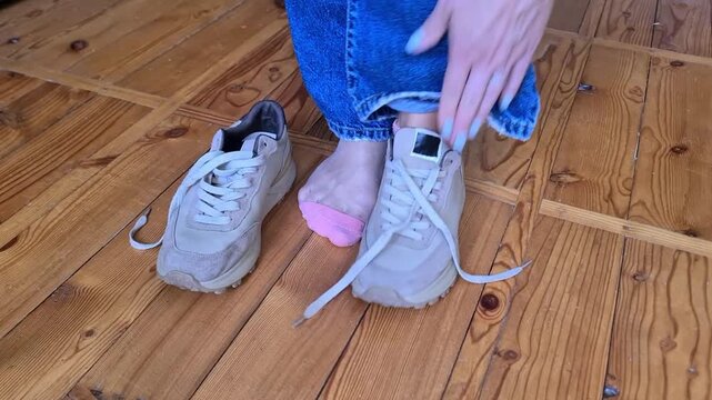 Person tying the laces of a sneaker while seated on a wooden floor indoors