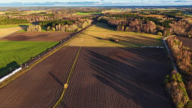 White train passing through rural autumn landscape with fields and forests. Modern and old 