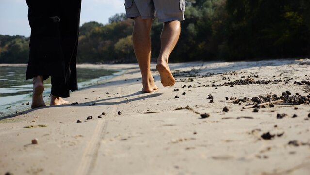 Bare feet of couple stepping together along sand beach at coastline. Male and female legs of pair walking near seaside. Happy lovers going along sandy shore. Concept of summer vacation or holiday