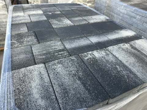 Wrapped pallet of dark grey concrete paving slabs outdoors