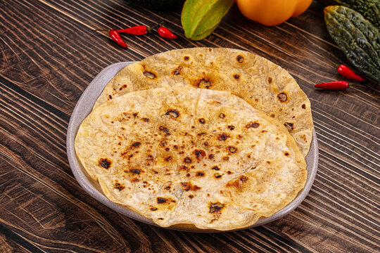 Grey plate holding two flatbreads with charred spots on dark wooden table with chili peppers and bitter melons