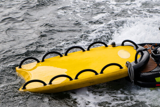 Bright yellow inflatable water rescue sled attached to a jet ski on choppy ocean water with white foam waves.