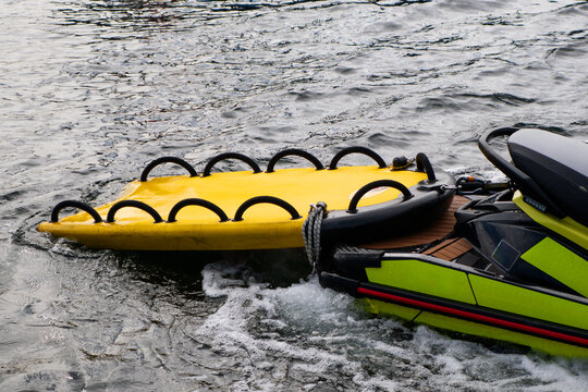 Bright yellow inflatable water rescue sled attached to a jet ski on choppy ocean water with white foam waves.