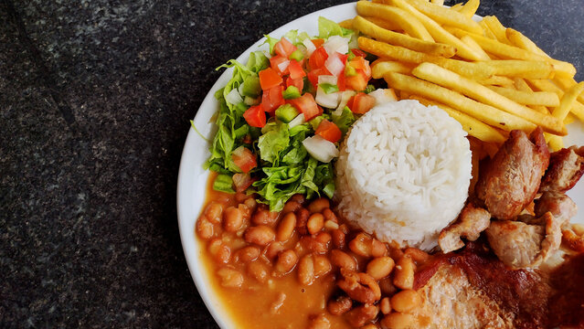 Hearty Brazilian Feijoada meal with rice beans french fries salad and meat on a white plate