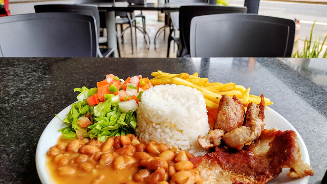 Delicious Brazilian prato feito meal with rice beans french fries salad and meat served on a white plate at a restaurant table