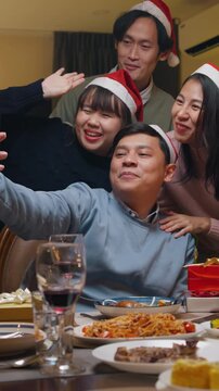 Vertical Screen : Group of Asia colleague gathering New year holidays party together. Happy friend group mobile phone video call online christmas thanksgiving dinner at home in evening.