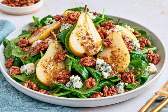 Fresh spinach salad with sliced pears, walnuts and blue cheese served with savory dressing on ceramic plate