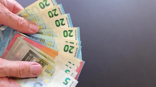 Hands fanning euro banknotes across dark neutral background showing bills spreading and movement only visible in scene - close-up of cash transaction action and currency detail