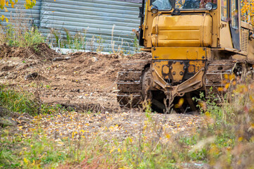 Heavy yellow industrial bulldozer or tractor on caterpillar tracks leveling ground and digging dirt during earthworks at a construction site © AileenK