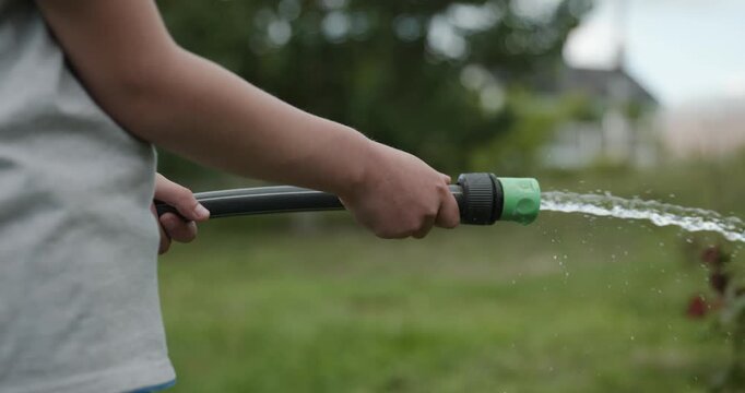 Close-up children hands watering plants in backyard. 4K 10-bit