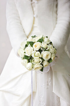 Bride in white dress and fur coat holding a classic rose wedding bouquet