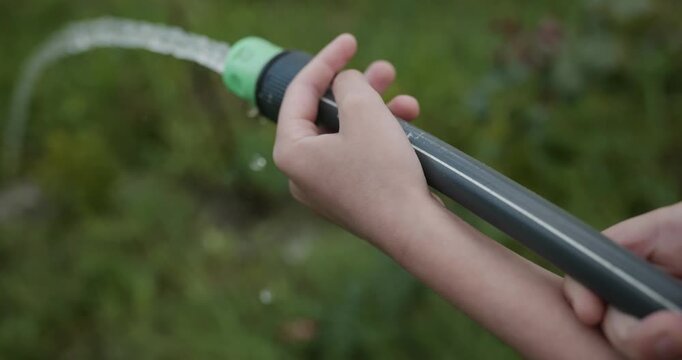 Close-up children hands watering plants in backyard. 4K 10-bit