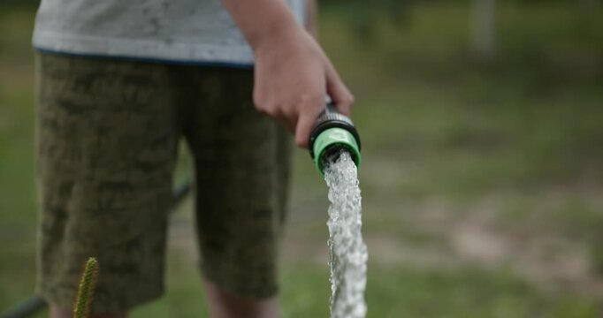 Close-up children hands watering plants in backyard. 4K 10-bit