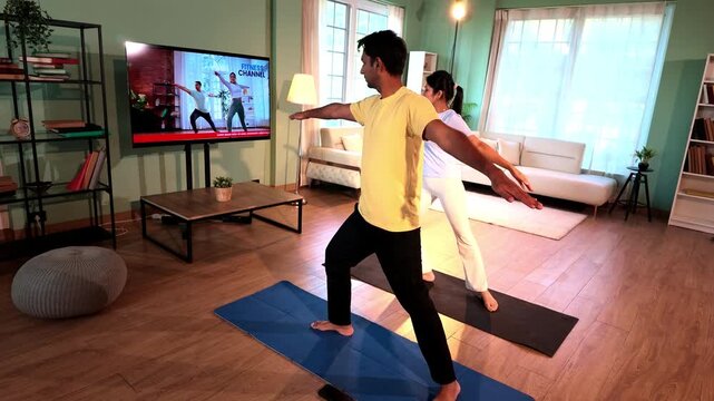 Young Indian couple performing bird dog yoga pose on exercise mats while following a TV tutorial in a lavish modern living room, improving balance, core strength and flexibility.