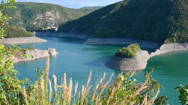 Wide scenic view of the Uvac reservoir between rounded green mountains in southwestern Serbia. Clear blue water, rocky shores and open sky create a peaceful natural landscape for travel concepts.
