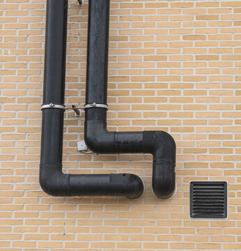 Black exterior ventilation pipes mounted on brick wall showing modern building systems.