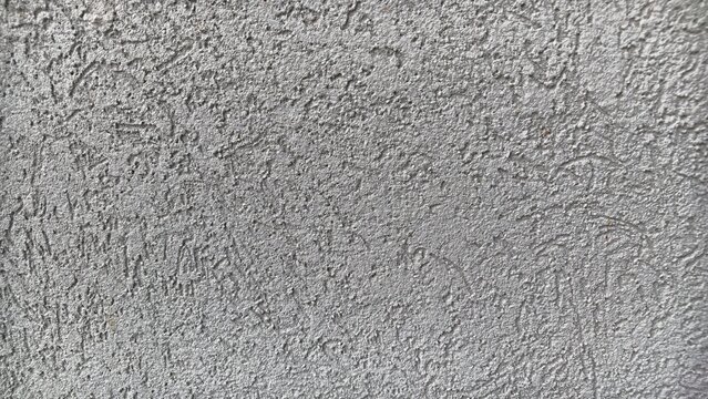 Gray rough stucco wall surface with coarse relief texture and scratched plaster pattern, full frame close-up of an exterior facade, construction and architecture background
