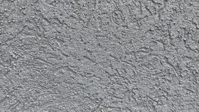 Gray rough textured stucco wall with raised swirls and irregular ridges, coarse plaster surface with uneven relief, full frame abstract background for design and construction use, close-up detail