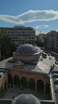 Cinematic vertical 9:16 aerial video, shot in smooth 60fps, pulling back from the newly restored Hamza Bey Mosque, also known as Alkazar, on the busy Egnatia Street in Thessaloniki.