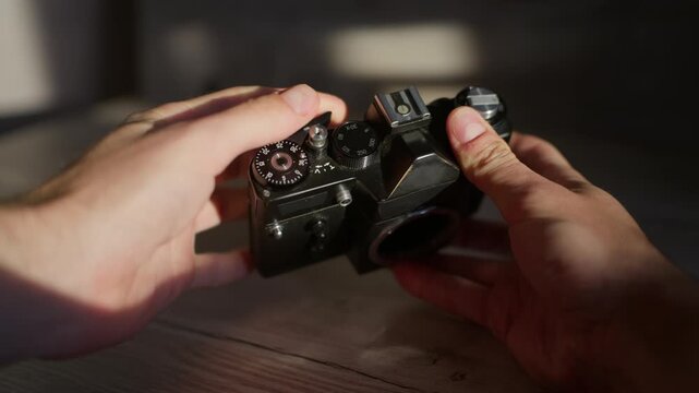 Photographer adjusts mechanical dials on a vintage analog body in a detailed close-up view. Sunlight illuminates the metallic top plate, exposure controls, and manual selector knobs.