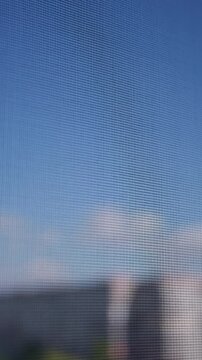 Window screen mesh texture overlooking clear blue sky in close-up. Shallow depth of field emphasizes the intricate grid pattern under soft natural daylight and serene atmospheric conditions.