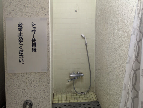 シャワー使用後は必ず止めてくださいの貼り紙 屋内プールのシャワーブースと混合水栓