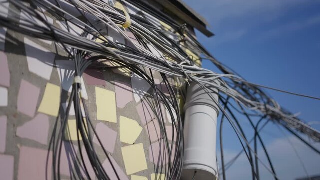 Bundled communication cables hang securely on a mosaic tile wall under daylight. Close details highlight tangled wire textures and colorful urban facade patterns against the sky.