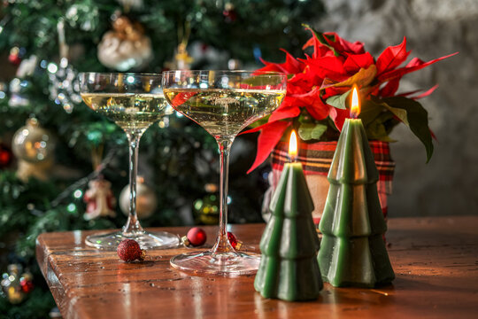 Champagne glasses and Christmas candles on a wooden table with poinsettia and festive tree